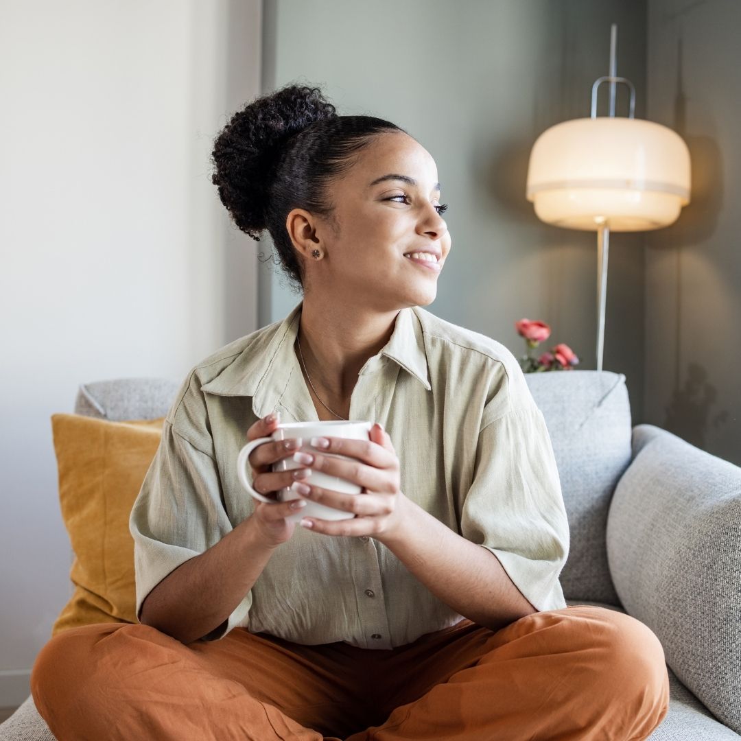 Person with calm expression holding a cup and sitting on couch