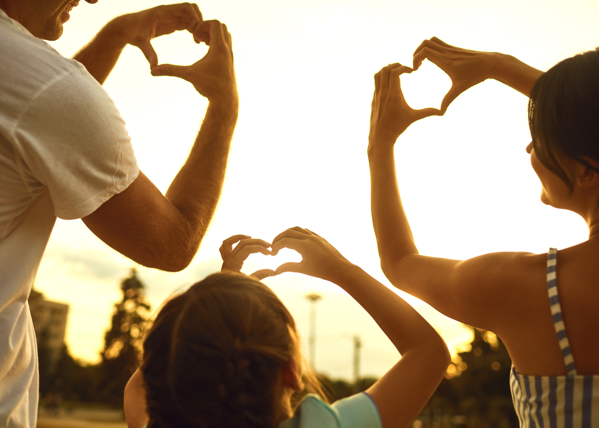 Two adults and one child making hearts of of their hands
