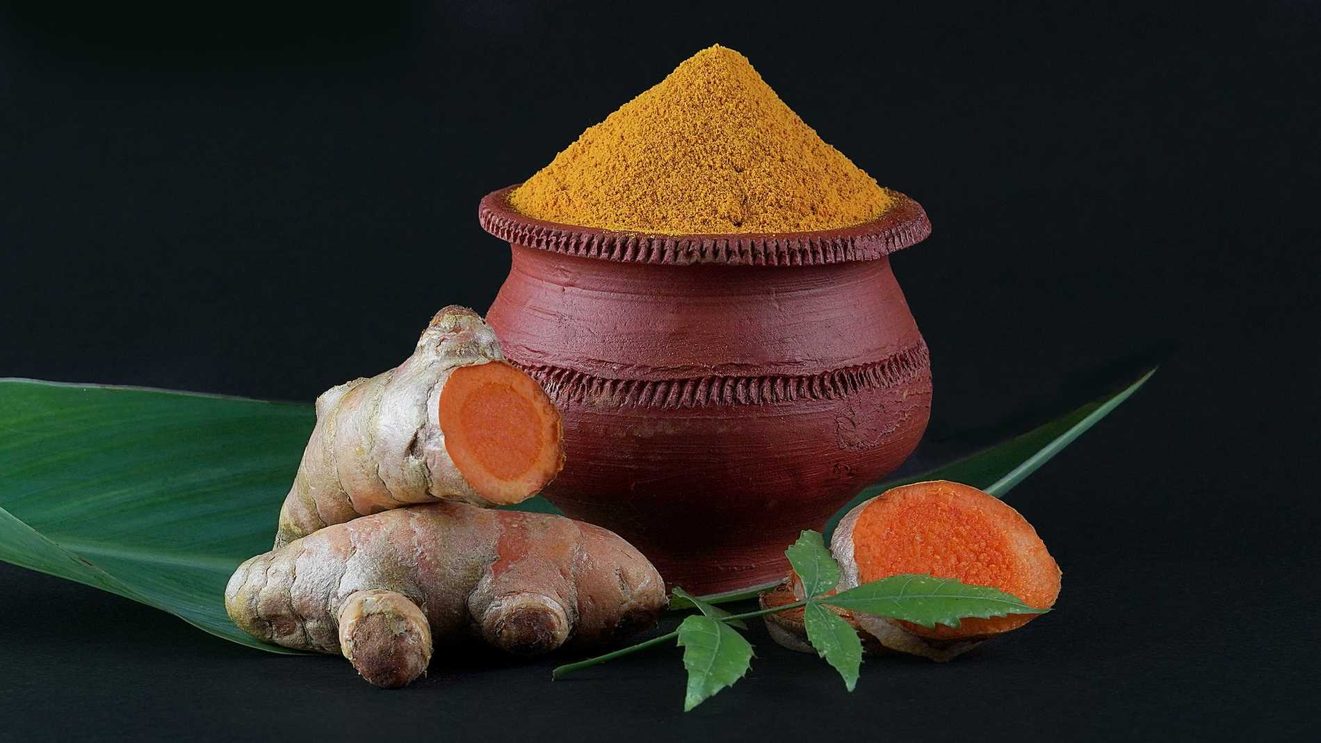 Bright orange flash and brown root of turmeric next to orange-yellow turmeric powder 