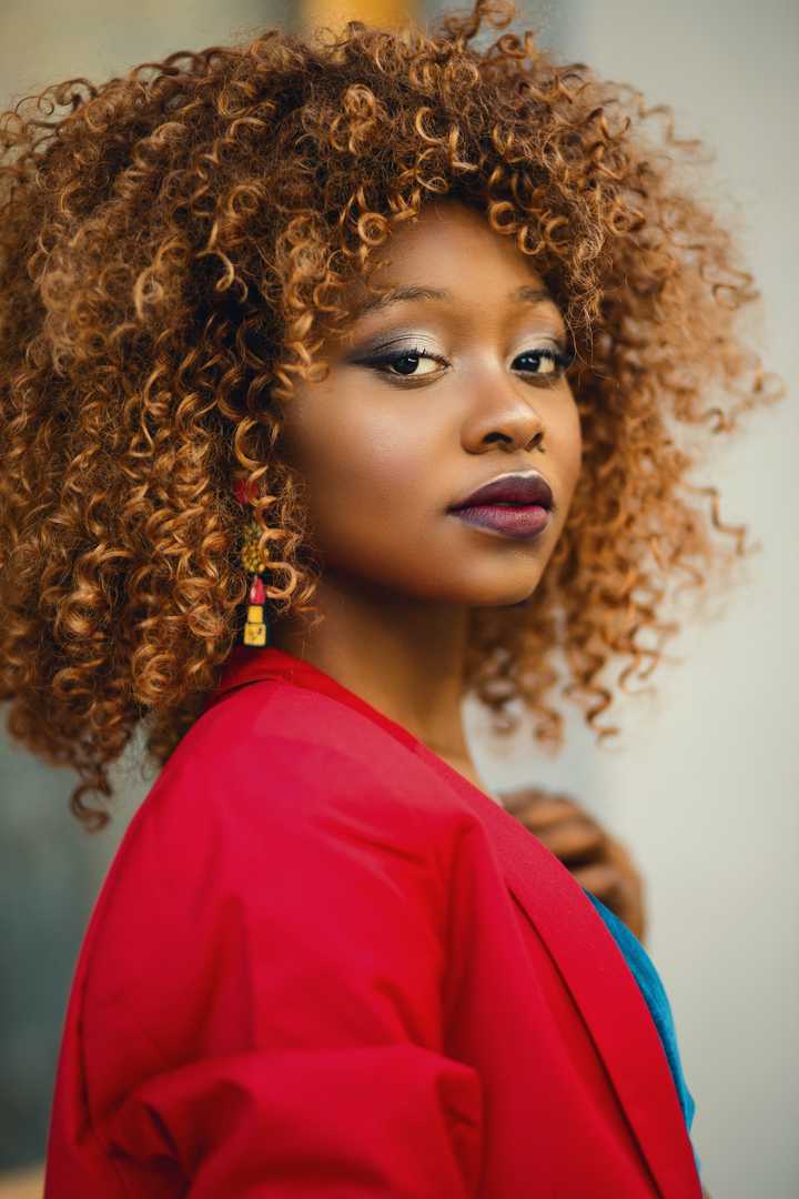 Curly-haired woman wearing earrings, red sweater and blue blouse