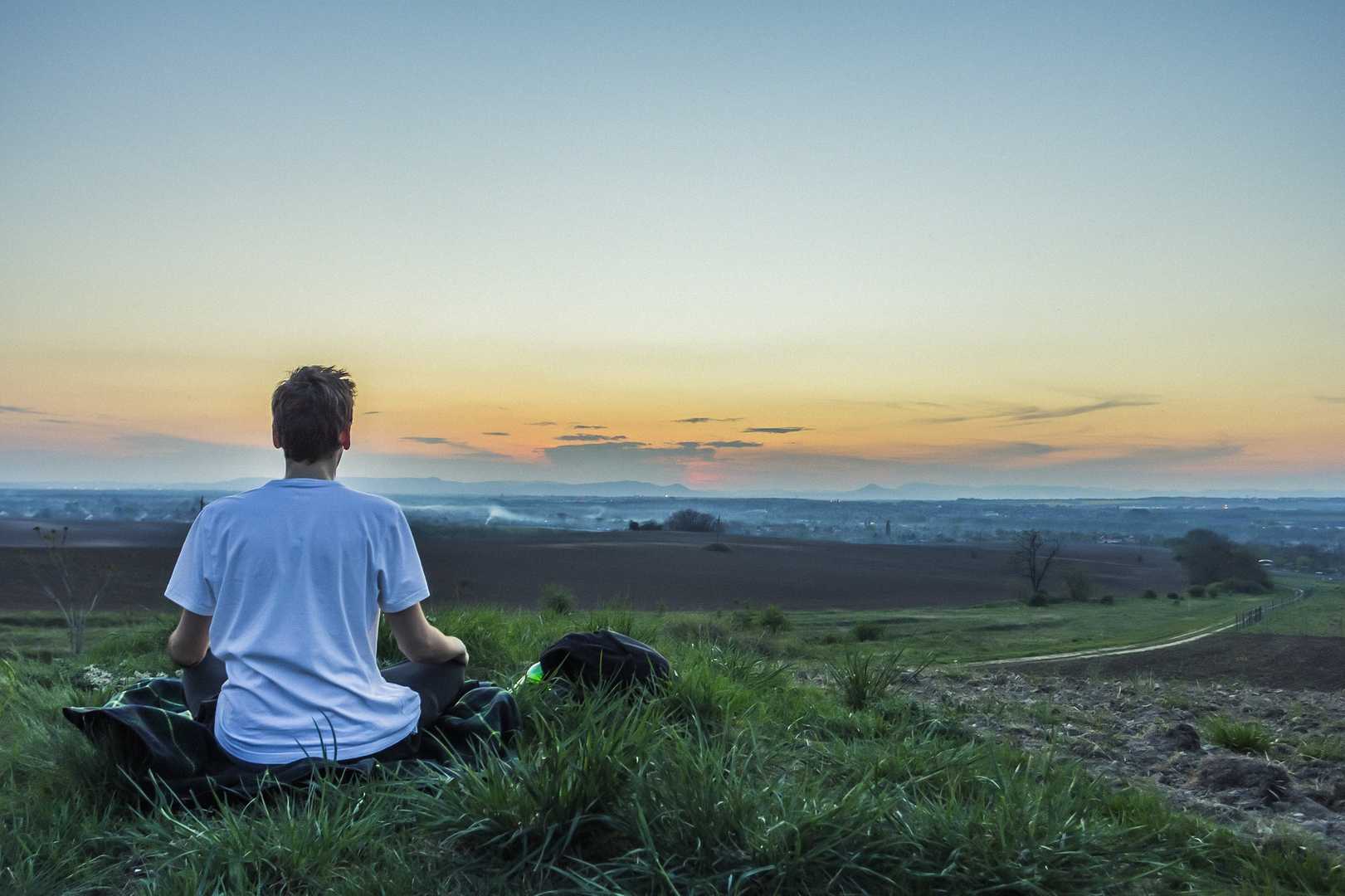 Person in white t-shirt meditating near the ocean at sunset